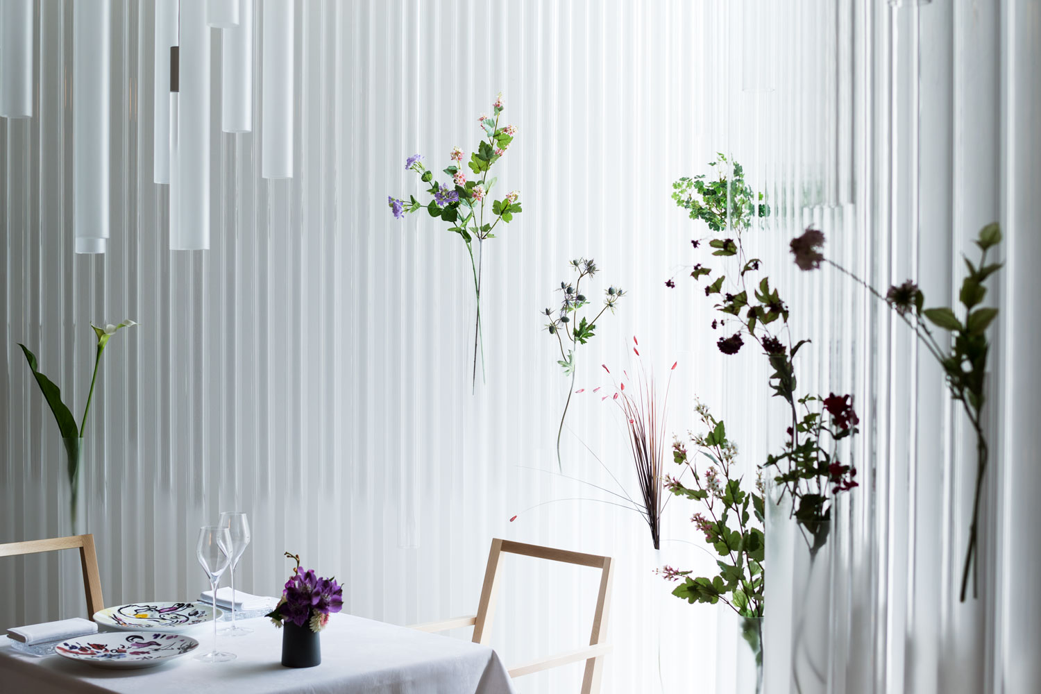 Tables set beneath the acrylic curtain, flowers visible inside the tubes