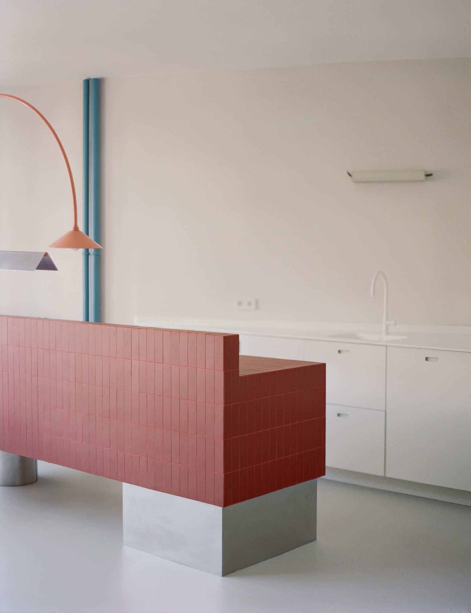 The restored flat: a tiled island on a raw concrete plinth, a blue column, and a tubular lamp in the colours the block was drawn in