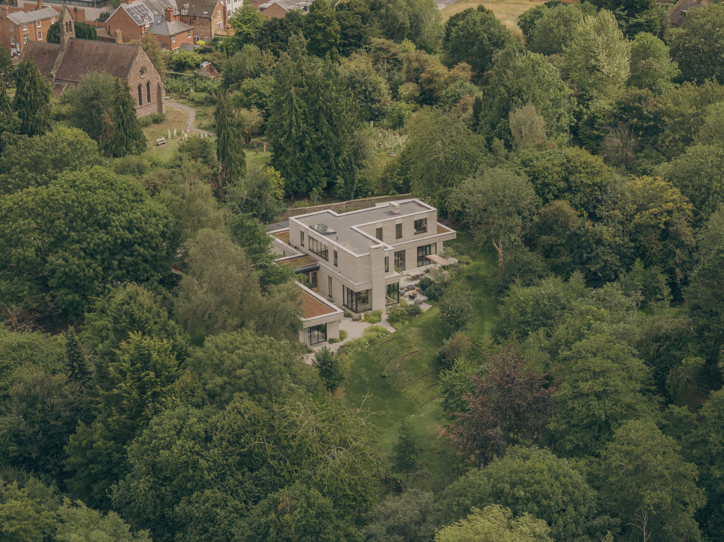 The F-shaped plan breaks the house into wings, and steps the upper floor back so it settles into the field instead of sitting on top of it.