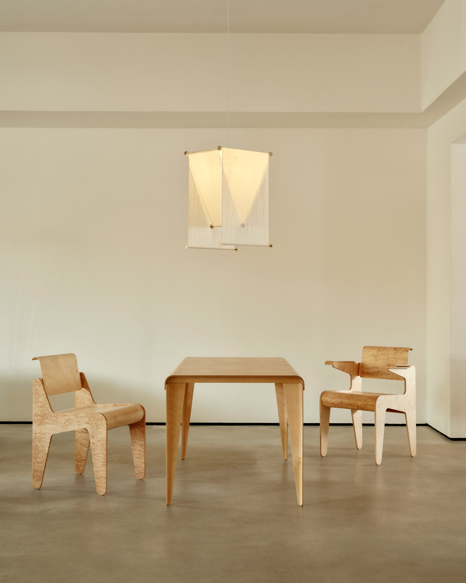 The Cut-Out Chair and Cut-Out Armchair in masur birch beneath a pendant lamp